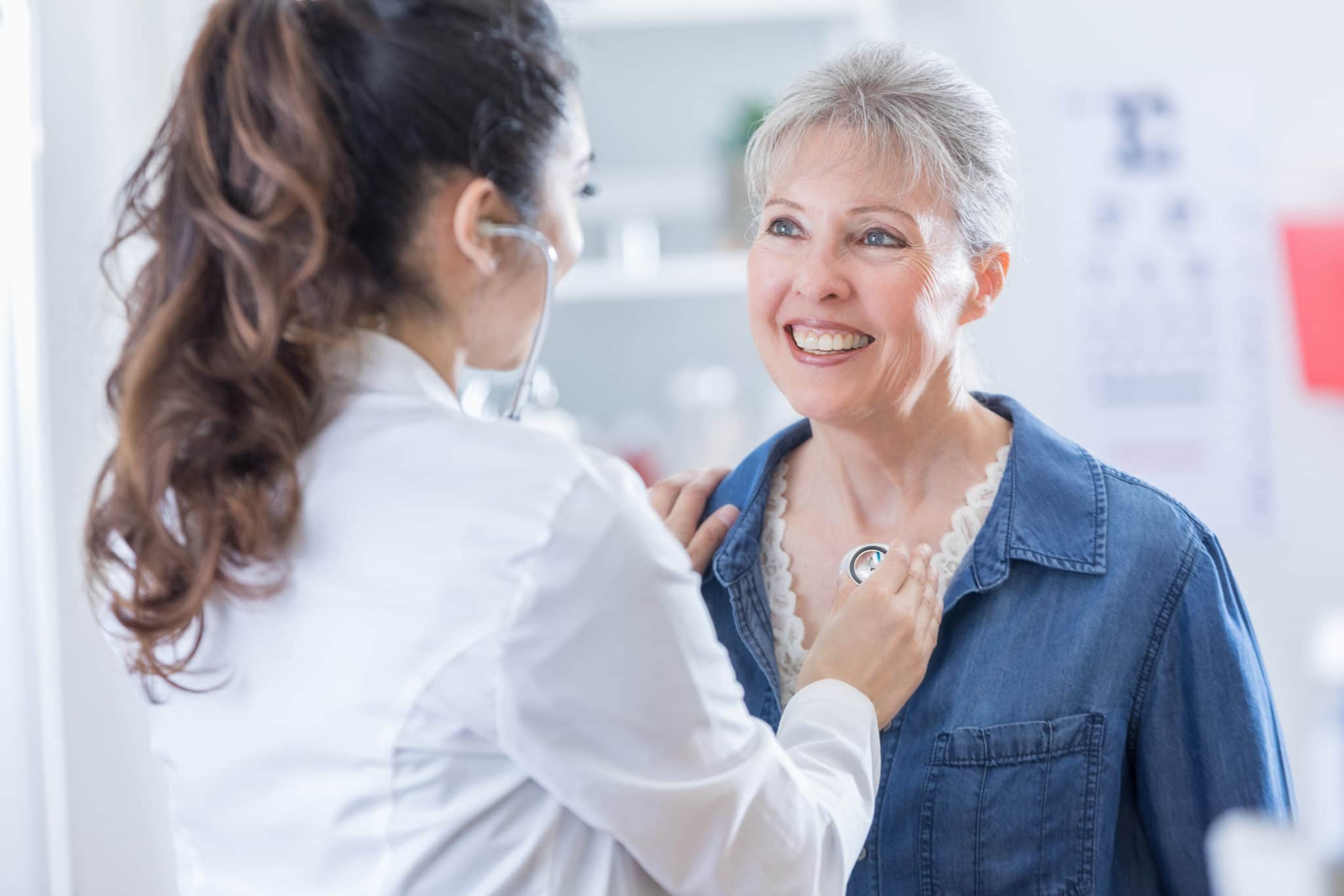 Female doctor listens to senior woman's heart during medical exam.