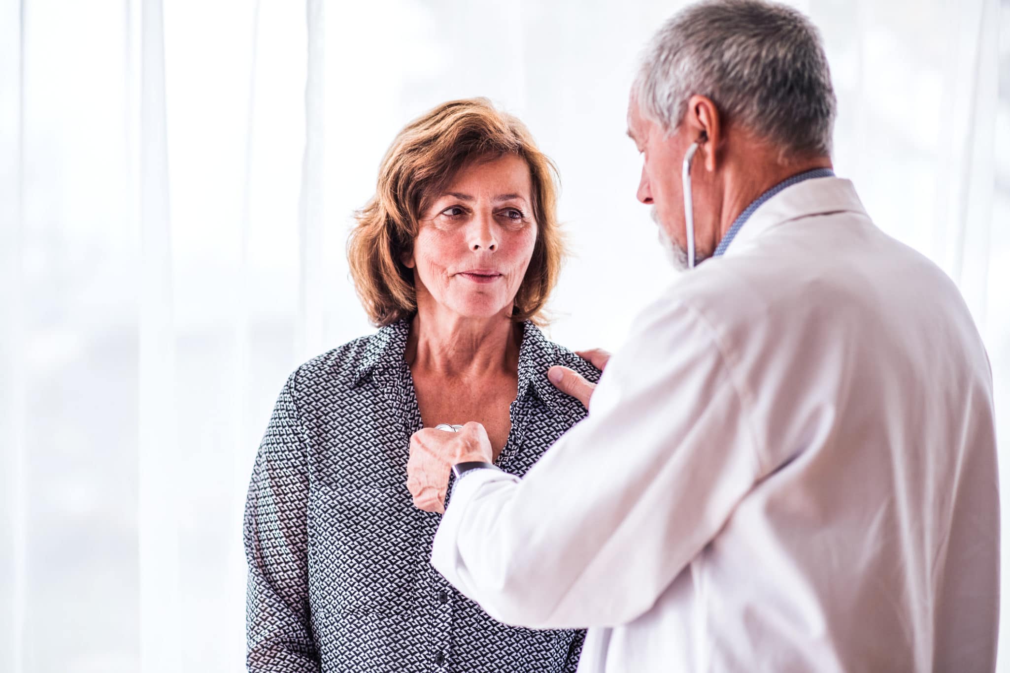 Male doctor examiming a senior woman in his office.